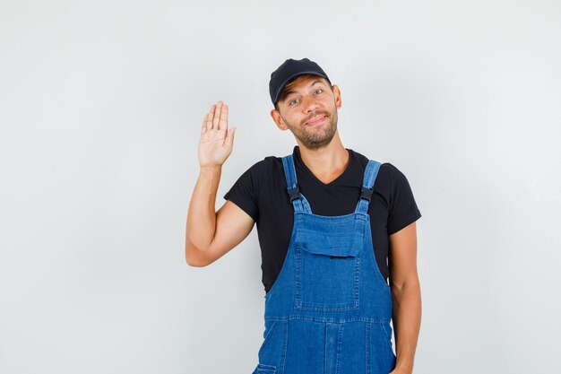 Jonge lader in uniform zwaaiende hand om afscheid te nemen en er gelukkig uit te zien, vooraanzicht.