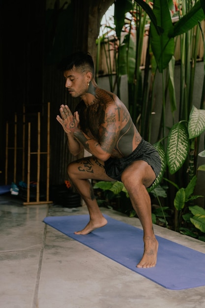 Jonge Latijns-Amerikaanse getatoeëerde man beoefent yoga buitenshuis tijdens retraitevakantie op Bali, stretching, meditatie, wellness