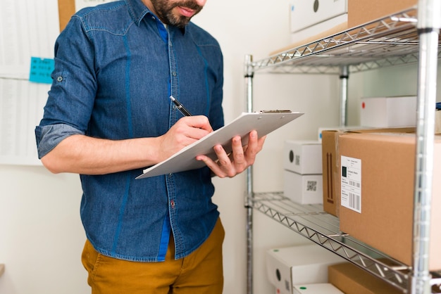 Gratis foto jonge latijns-man en ondernemer met veel bestellingen in zijn online winkel. bedrijfseigenaar schrijft klantinformatie op een klembord