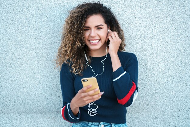 Jonge latijnse vrouw die lacht terwijl ze haar mobiele telefoon buiten op straat gebruikt. Stedelijk begrip.