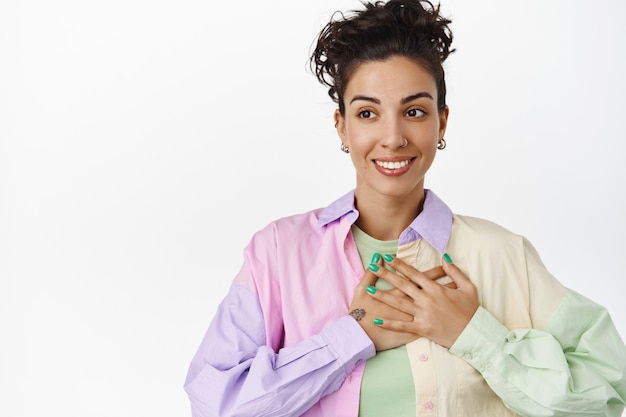 Jonge lesbische vrouw die hand op het hart houdt, gelukkig glimlacht en wegkijkt naar logo, wordt verheven, trots en lgbtq-concept op wit geïsoleerd
