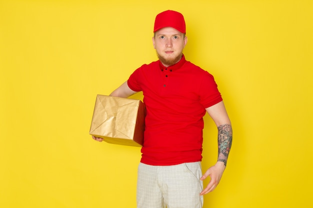 jonge levering man in rode polo rode dop witte jeans met een doos op geel