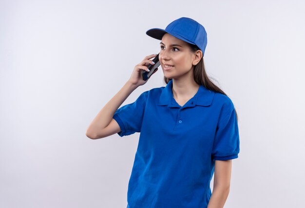 Jonge levering meisje in blauw uniform en pet glimlachen tijdens het gesprek op de mobiele telefoon