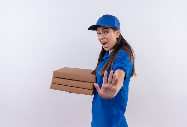 Jonge levering meisje in blauw uniform en pet houden pizzadozen stopbord met hand met angst expressie op gezicht maken
