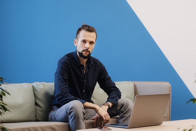 Jonge man aan het werk op de laptop zittend op de bank in het kantoor