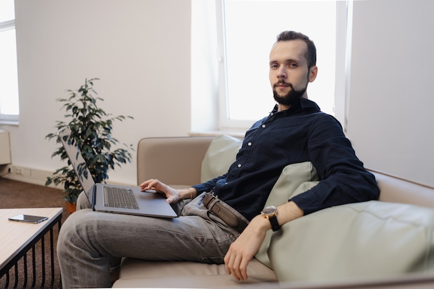 Jonge man aan het werk op de laptop zittend op de bank in het kantoor