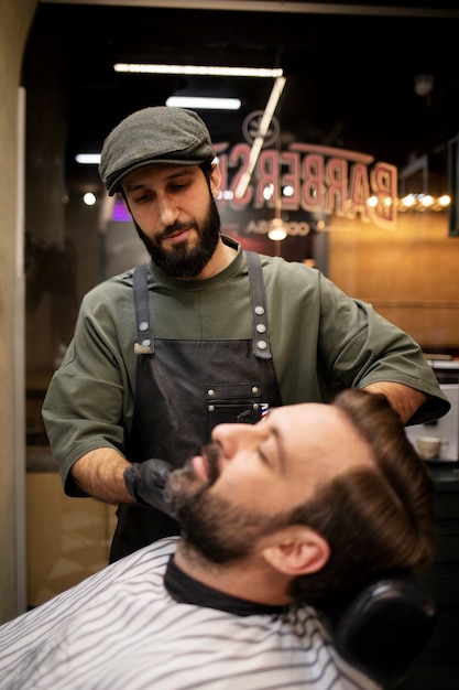 Gratis foto jonge man bij de kapper die zijn baard laat trimmen