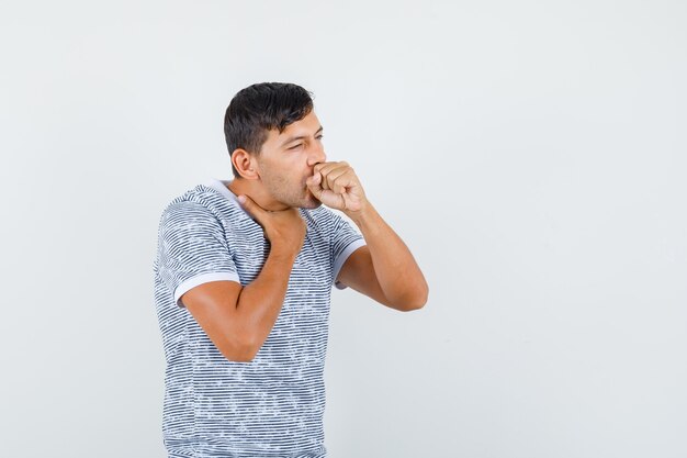 Jonge man die aan hoest in t-shirt lijdt en ziek kijkt