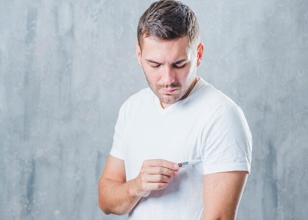 Jonge man die de medische digitale thermometer in zijn onderarm