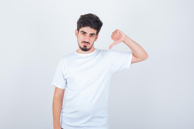 Jonge man die duim naar beneden in een wit t-shirt laat zien en er zelfverzekerd uitziet