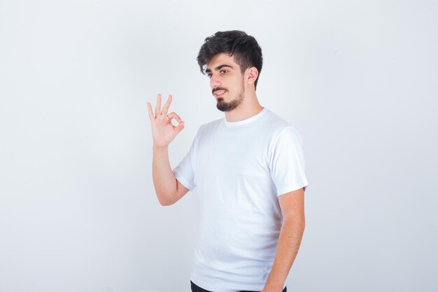 Jonge man die een goed gebaar toont in een wit t-shirt en er zelfverzekerd uitziet