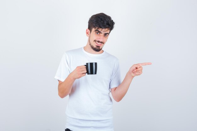 Jonge man die een kopje drank vasthoudt, opzij wijst in een wit t-shirt en er zelfverzekerd uitziet