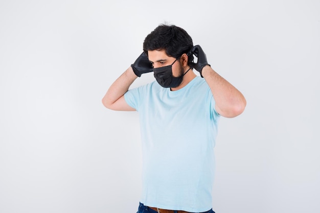 Jonge man die een medisch masker en handschoenen in een t-shirt draagt en er verstandig uitziet. vooraanzicht.