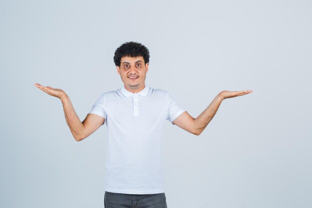 Jonge man die een verwelkomend gebaar toont in een wit t-shirt, een broek en er zelfverzekerd uitziet. vooraanzicht.