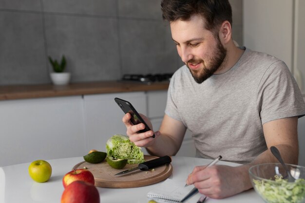Jonge man die eet en zijn smartphone controleert