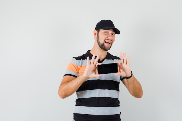 Jonge man die foto op mobiele telefoon in t-shirt, pet en op zoek vrolijk.