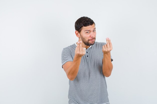 Jonge man die geldgebaar in t-shirt toont en er behoeftig uitziet. vooraanzicht.