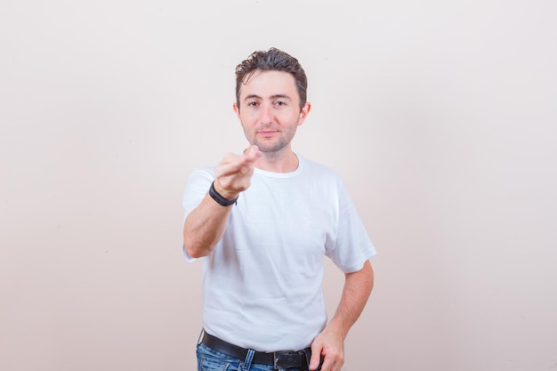 Jonge man die hand en vingers in wit t-shirt, spijkerbroek uitrekt en er zelfverzekerd uitziet