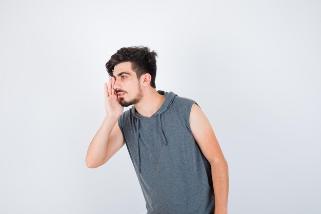 Jonge man die hand in de buurt van mond houdt terwijl hij iemand in een grijs t-shirt belt en er serieus uitziet?