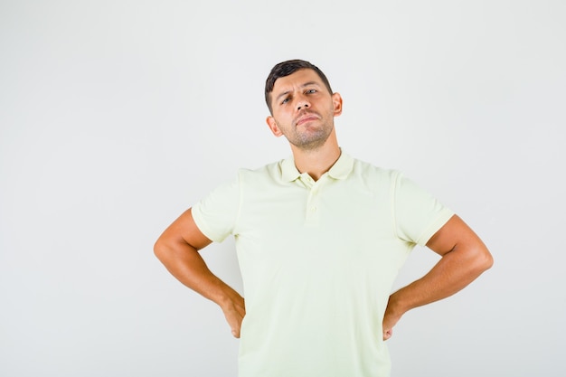 Jonge man die met de handen op zijn taille in t-shirt staat en zelfverzekerd kijkt.