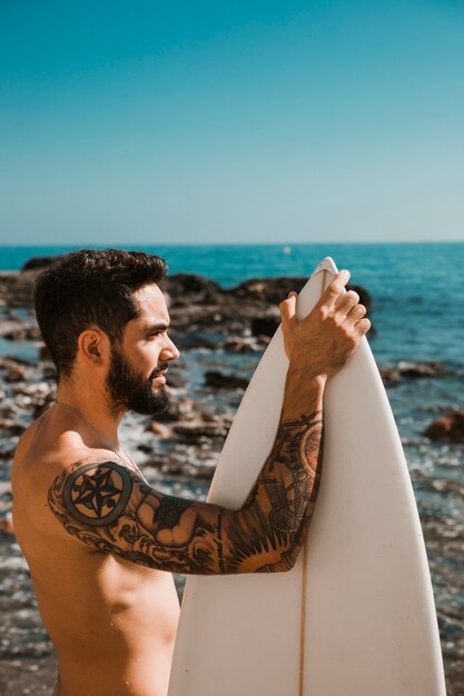 Jonge man die met witte surfplank op het strand