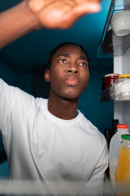 Gratis foto jonge man die midden in de nacht de koelkast thuis opent voor een snack