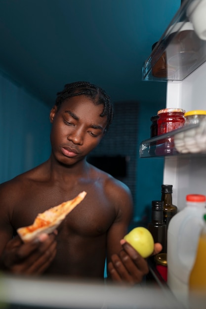 Jonge man die midden in de nacht de koelkast thuis opent voor een snack