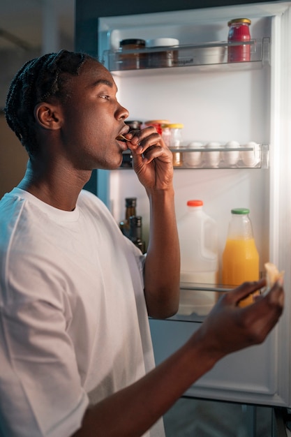 Gratis foto jonge man die midden in de nacht thuis naast de koelkast een snack eet