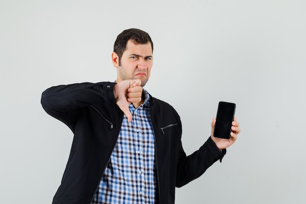 Jonge man die mobiele telefoon houdt, duim in overhemd, jasje toont en somber kijkt