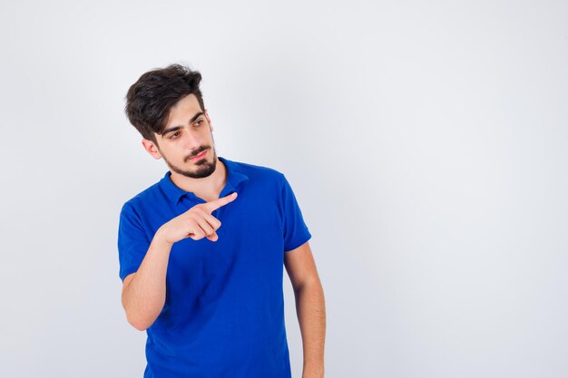 Jonge man die naar rechts wijst met wijsvinger in blauw t-shirt en er serieus uitziet