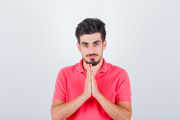 Jonge man die namaste-gebaar in roze t-shirt toont en er verstandig uitziet. vooraanzicht.