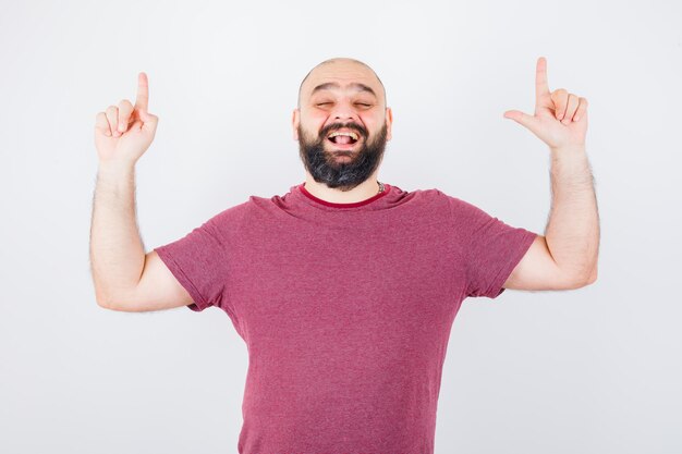 Jonge man die omhoog wijst terwijl hij in een roze t-shirt glimlacht en er vrolijk uitziet. vooraanzicht.