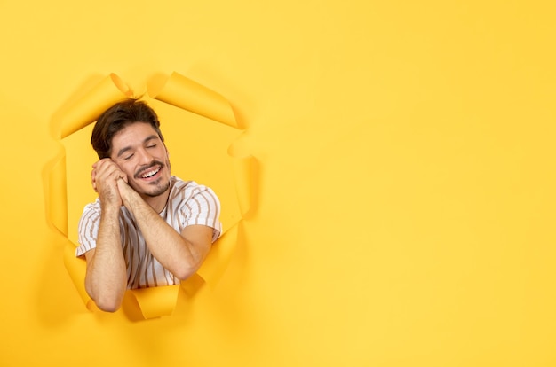 Jonge man die op gescheurde gele papieren achtergrond kijkt en staat, man indoor sale gezichtsbehandeling