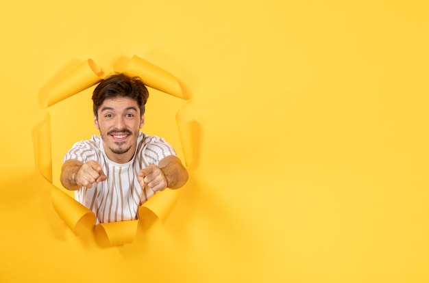 Jonge man die op gescheurde gele papieren achtergrond kijkt en staat voor gezichtsbehandeling binnenshuis