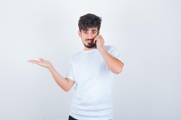 Jonge man die op mobiele telefoon praat terwijl hij de palm in een t-shirt spreidt en er zelfverzekerd uitziet