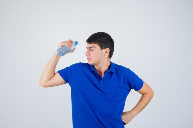 Jonge man die plastic fles houdt terwijl hij hand op taille in t-shirt houdt en er zelfverzekerd uitziet. vooraanzicht.