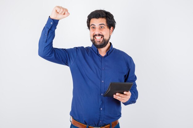 Jonge man die rekenmachine vasthoudt terwijl hij het gebaar van de winnaar in het vooraanzicht van het koningsblauwe shirt toont.