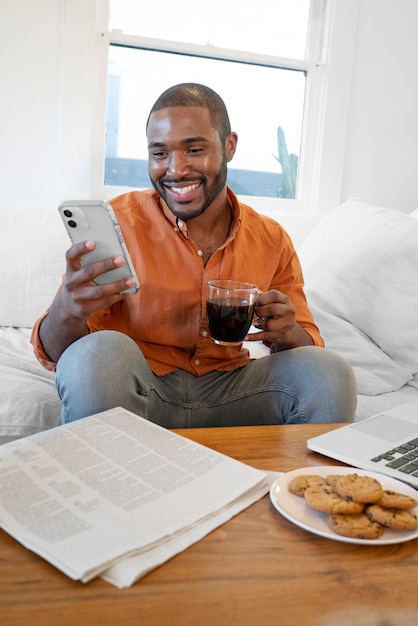 Gratis foto jonge man die smartphone gebruikt terwijl hij thuis een kopje koffie drinkt