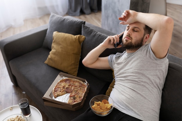 Jonge man die thuis op de bank junkfood eet