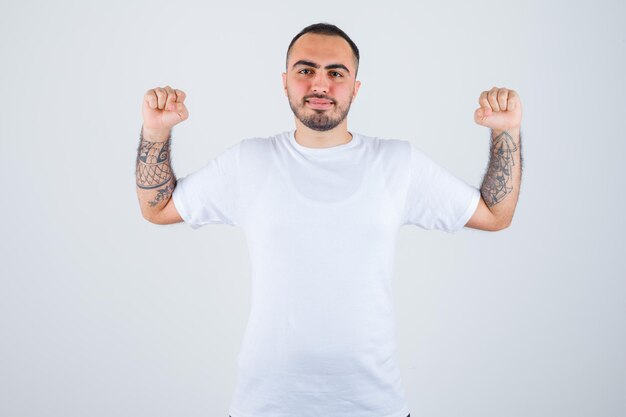 Jonge man die winnaargebaar in wit t-shirt toont en er gelukkig uitziet