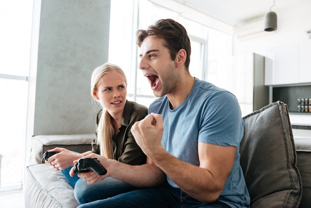 Jonge man die winnaargebaar toont terwijl het spelen met zijn vrouw in videospelletjes