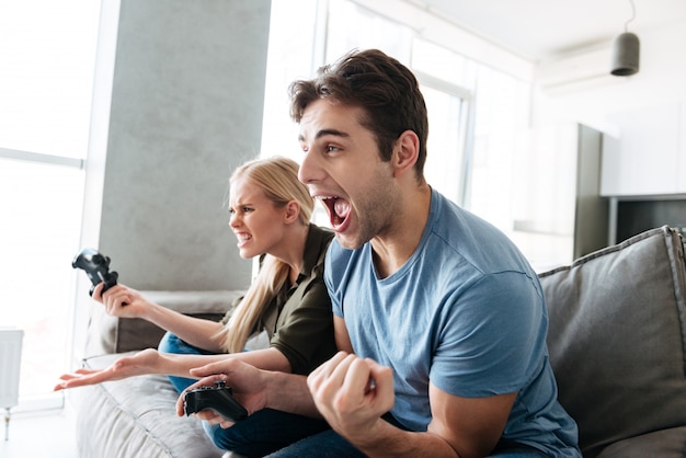 Jonge man die winnaargebaar toont terwijl het spelen met zijn vrouw in videospelletjes