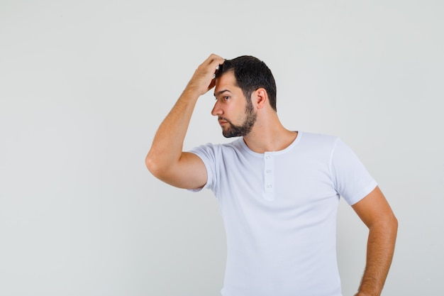 Jonge man die zich voordeed terwijl hij hand op zijn voorhoofd in t-shirt houdt en er cool uitziet. vooraanzicht.