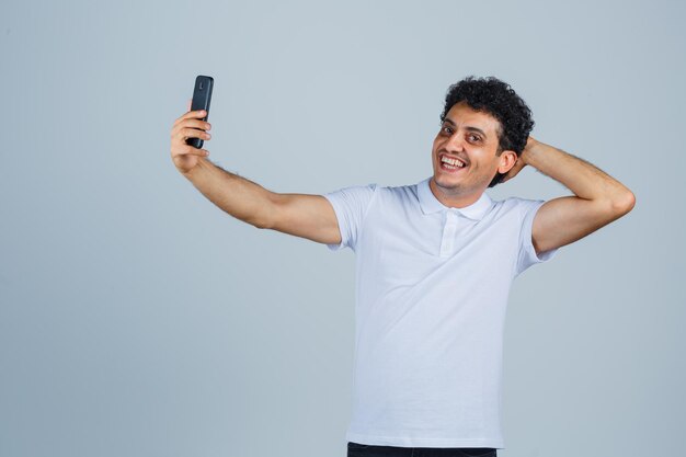 Jonge man die zich voordeed terwijl hij selfie in wit t-shirt nam en er gelukkig uitzag. vooraanzicht.