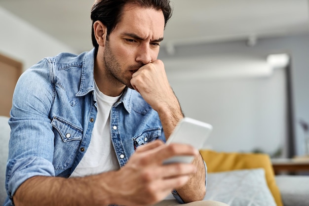 Jonge man die zich zorgen maakt tijdens het lezen van een sms-bericht op een mobiele telefoon thuis