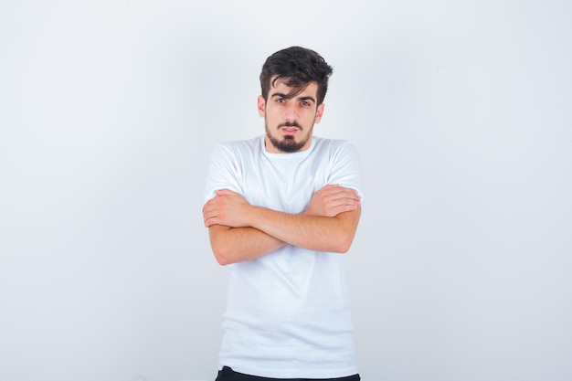 Jonge man die zichzelf omhelst of het koud heeft in een wit t-shirt en er verstandig uitziet