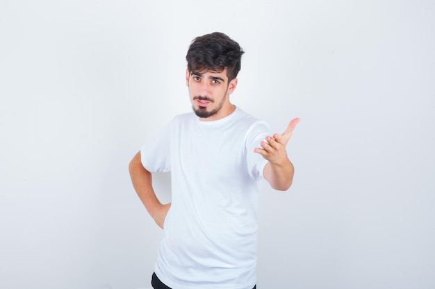 Jonge man die zijn hand opsteekt in een vragende pose in een t-shirt en er zelfverzekerd uitziet