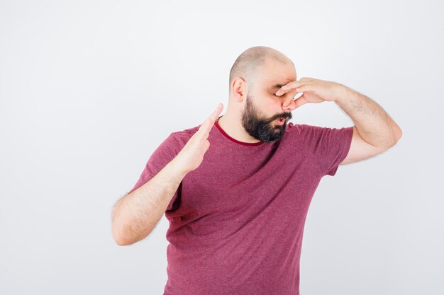 Jonge man die zijn linkerhand op de elleboog houdt, aan iets denkt in een roze t-shirt en er geïrriteerd uitziet, vooraanzicht.