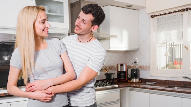 Jonge man die zijn vriendin omhelst die elkaar in de keuken bekijkt