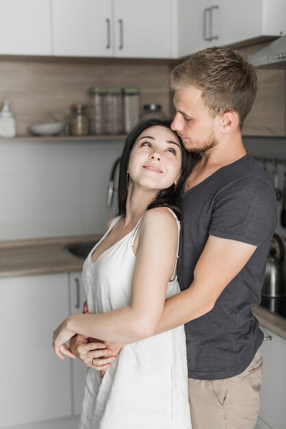 Jonge man die zijn vrouw omhelst die zich in de keuken bevindt